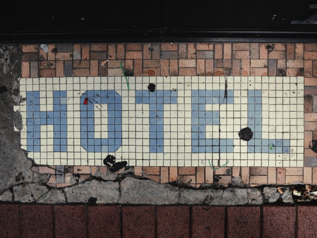 A close-up view of a vintage hotel sign in blue on a mosaic floor, with signs of weathering and age.